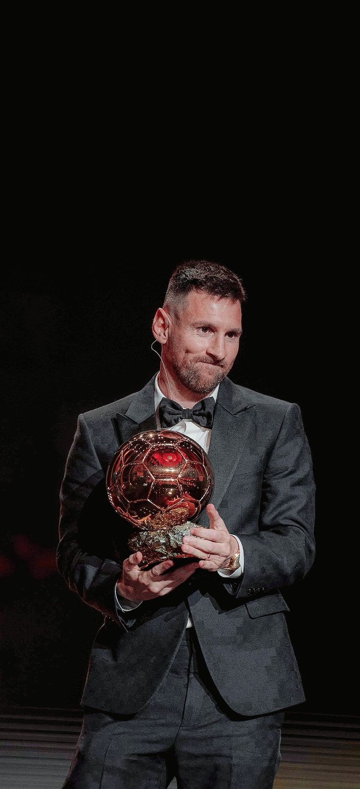 a man in a suit and bow tie holding a ballon d'or award