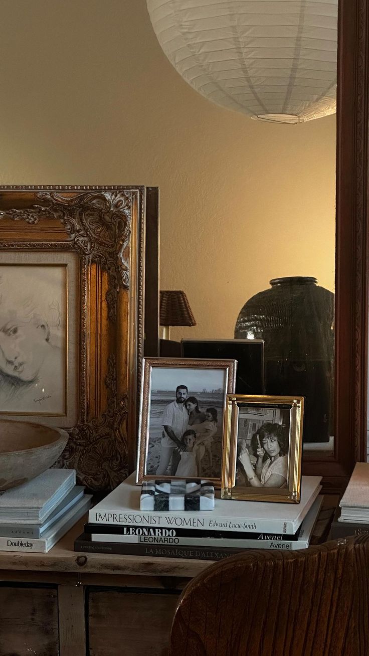 a table with books and pictures on it in front of a framed photograph next to a lamp