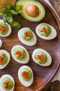 deviled eggs topped with guacamole and garnish on a wooden platter