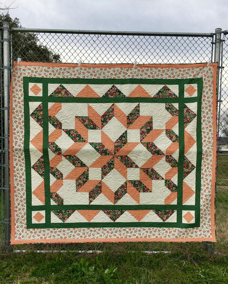 an orange and green quilt hanging on a chain link fence