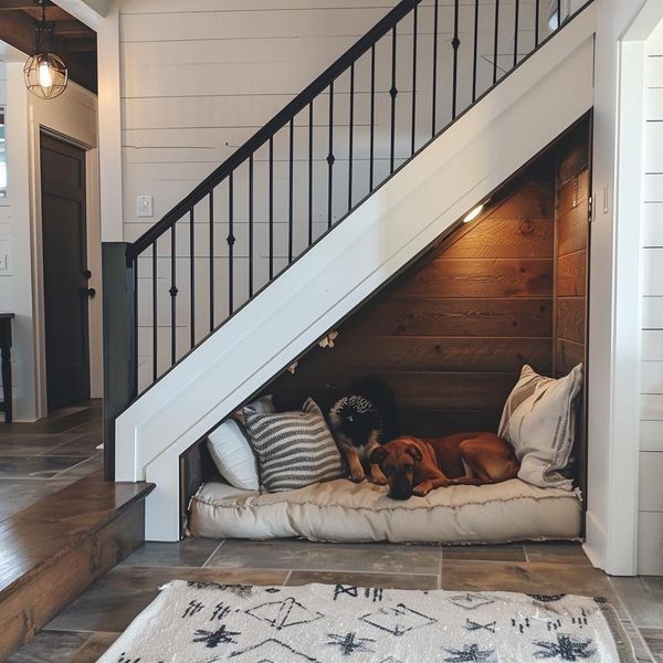 two dogs sleeping in their dog bed under the stairs