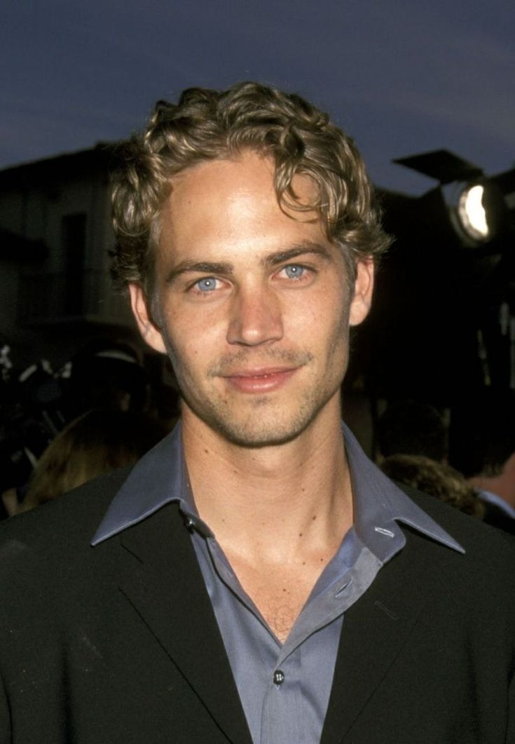 a man with curly hair and blue eyes is posing for a photo in front of a camera