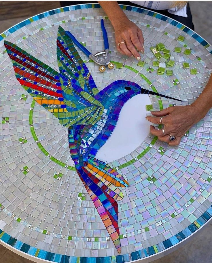 a bird made out of mosaic tiles sitting on top of a glass table topped with scissors