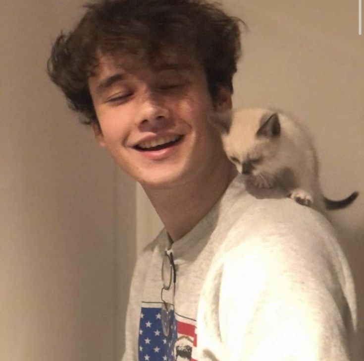 a young man holding a cat on his shoulder