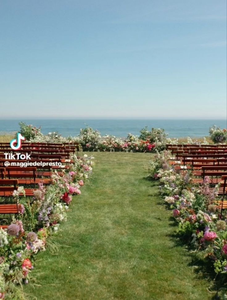 rows of wooden benches sitting on top of a lush green field next to the ocean