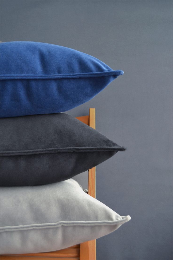 four pillows stacked on top of each other in front of a gray wall and wooden chair