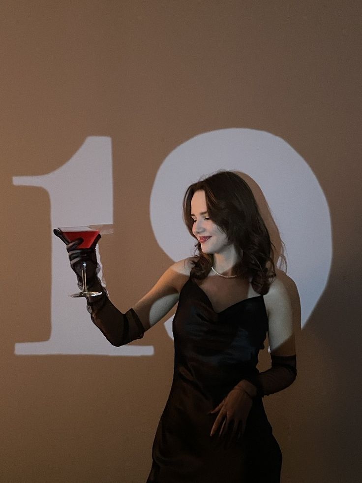 a woman in a black dress holding up a red glass with the number ten on it