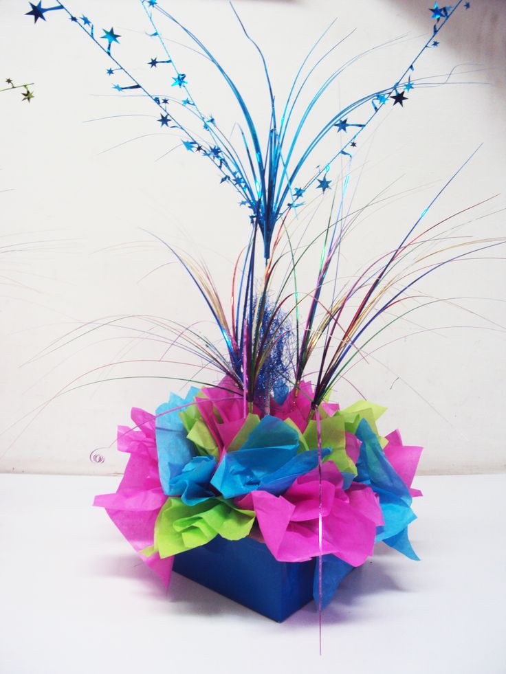 a blue vase filled with lots of colorful flowers on top of a white table next to a wall