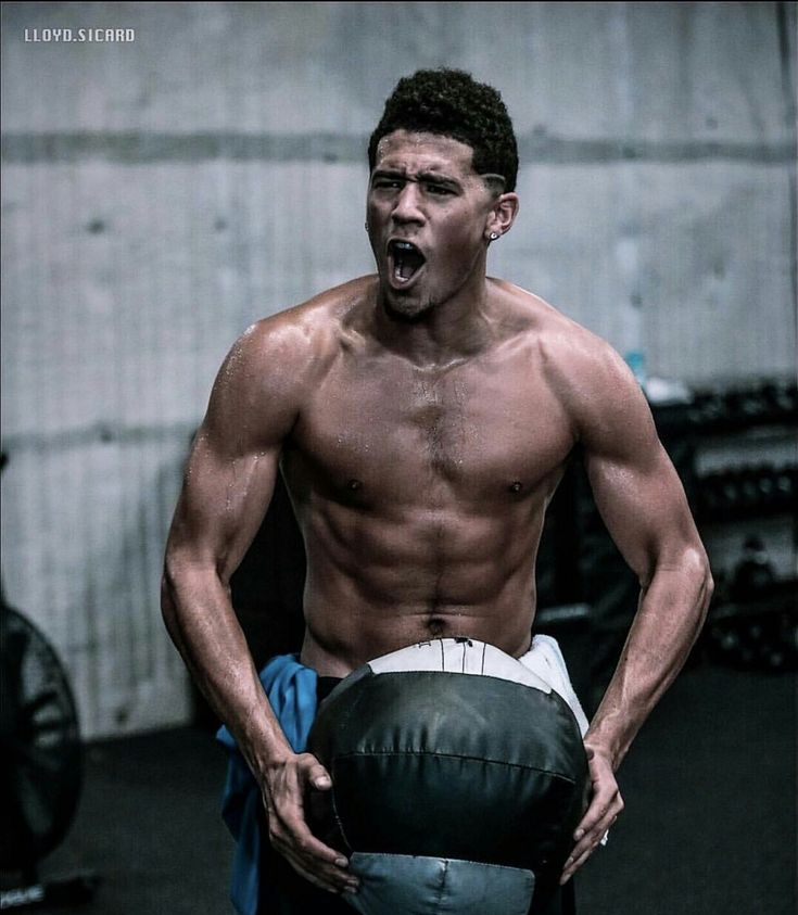 a shirtless man holding a medicine ball and making a face with his mouth wide open