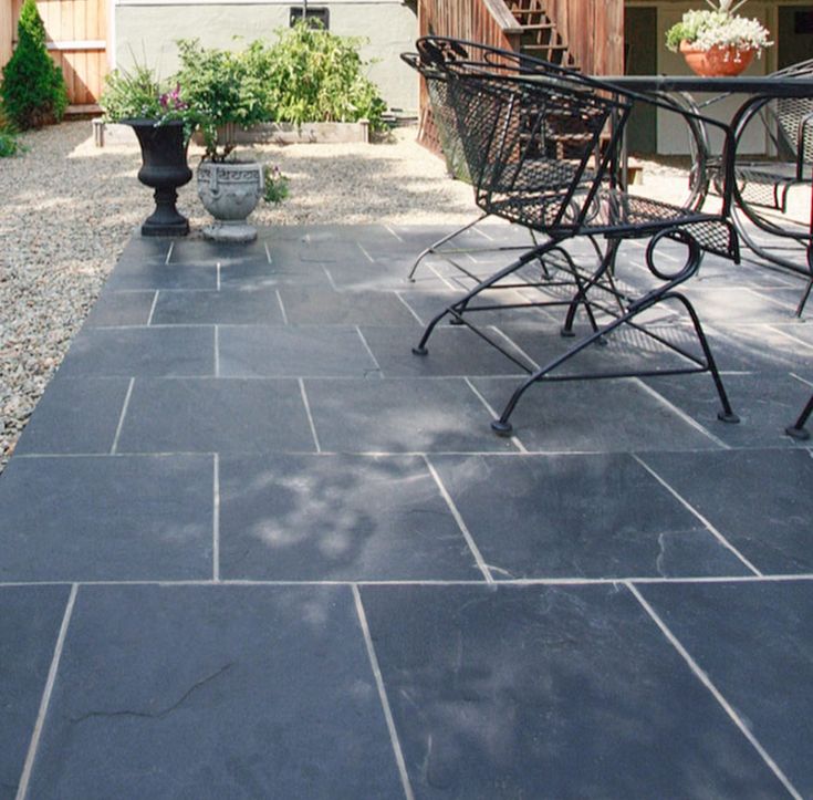 a patio with chairs and potted plants on the ground in front of a house