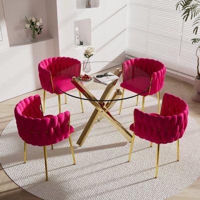 a round glass table with pink chairs and a white rug on the floor in front of it