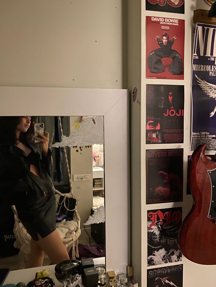 a woman standing in front of a mirror next to a guitar