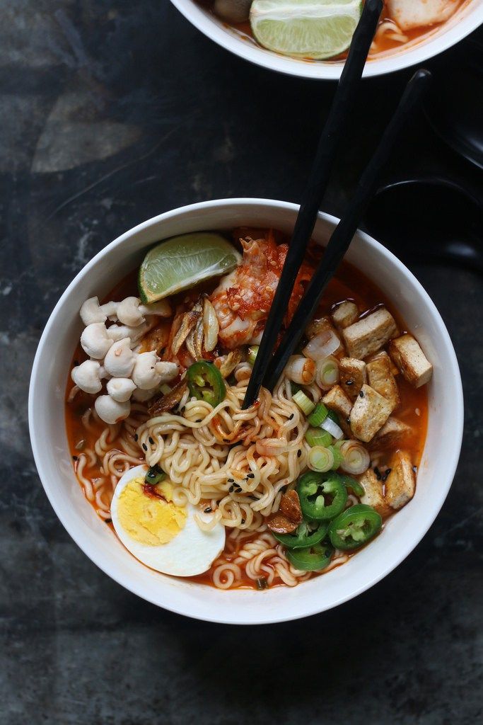 two bowls of noodles with chopsticks and an egg on the side, sitting on a table