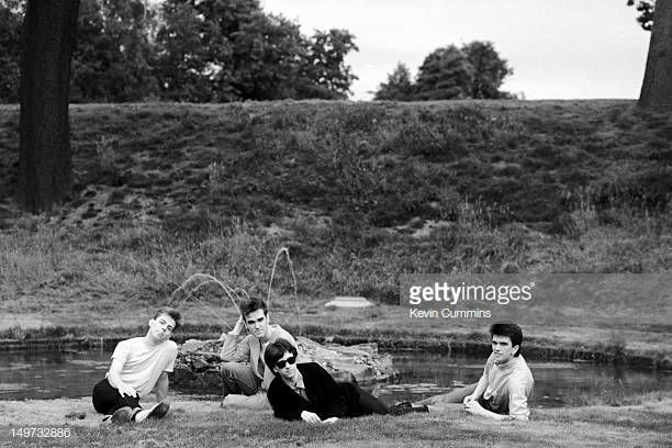 four people sitting on the ground next to a body of water with trees in the background