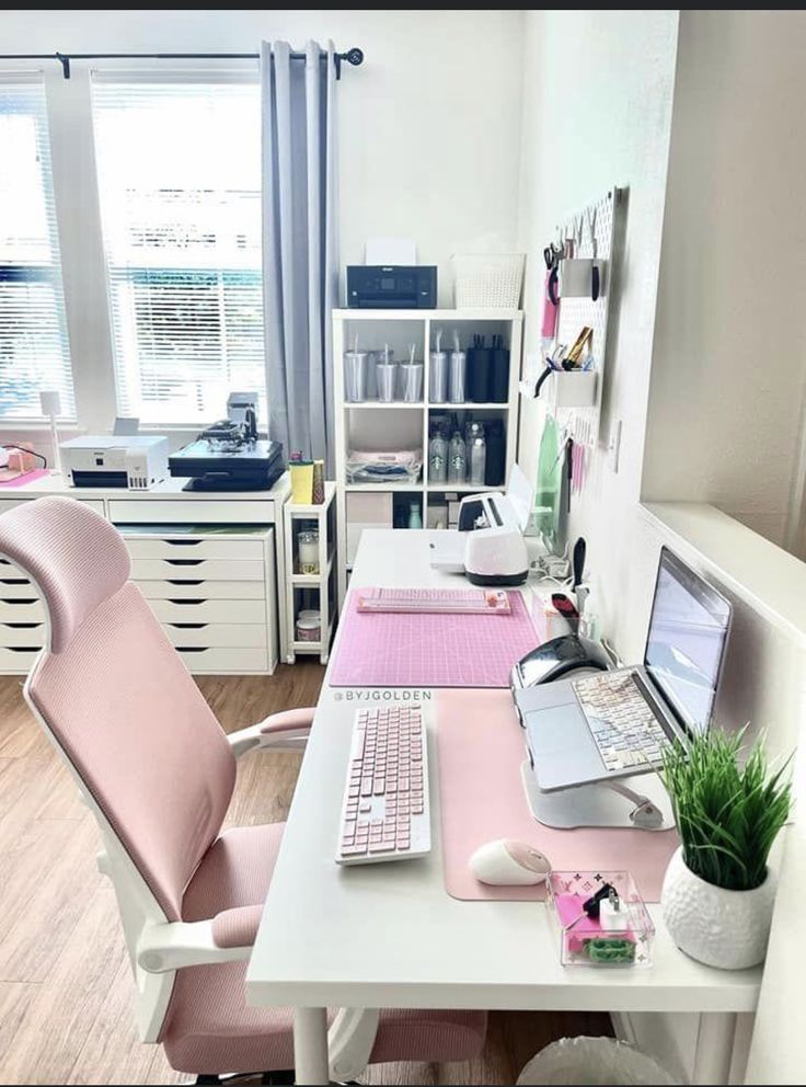 a desk with a computer, keyboard and plant on it in front of a window