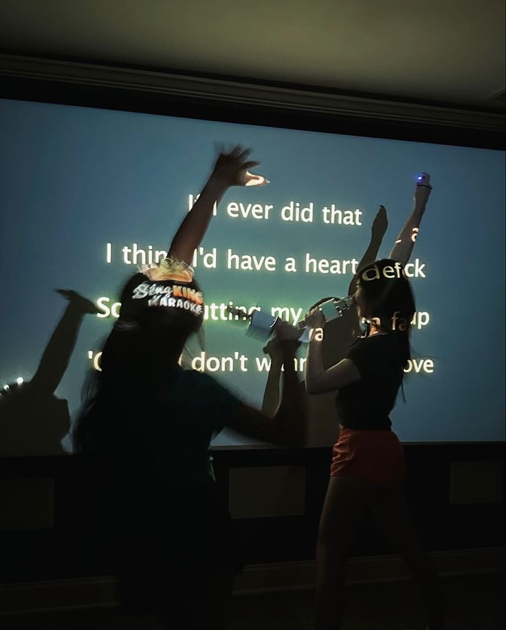 two people standing in front of a projection screen with their hands up to the sky