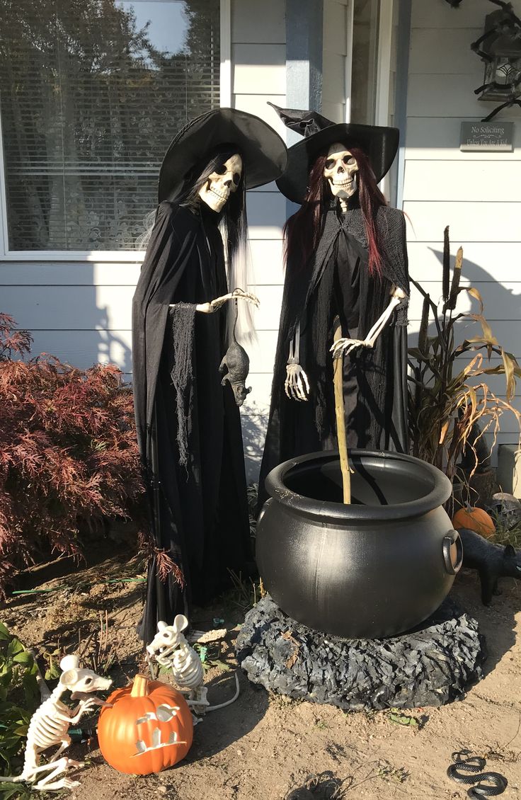 two skeletons dressed in black standing next to a caulder with a witch inside