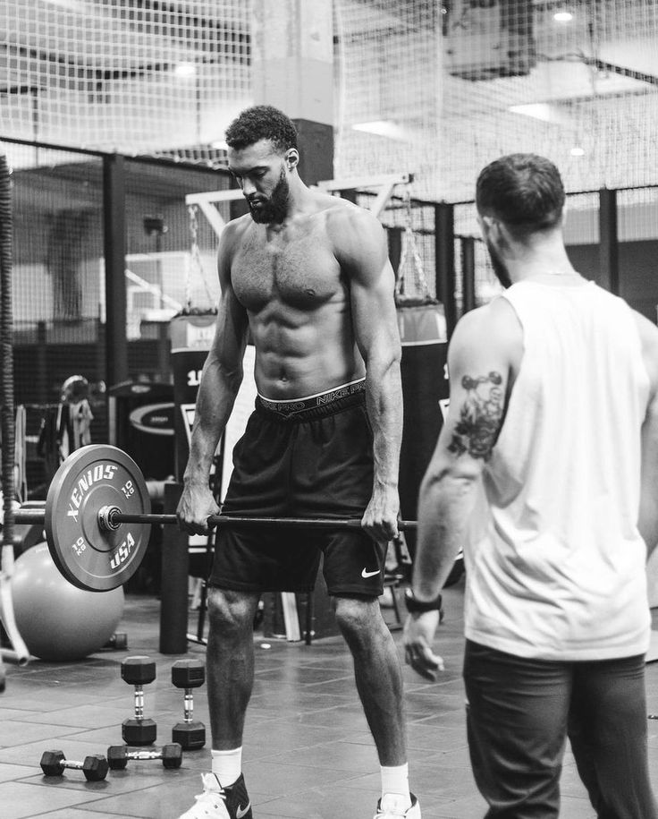 a shirtless man holding a barbell while standing next to another man in a gym