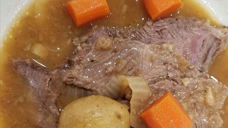 a white plate topped with meat, potatoes and carrots on top of broth