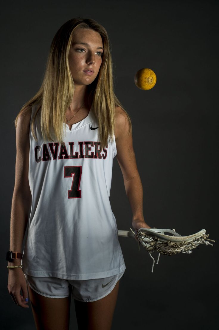 a woman in a white jersey holding a lacrosse ball and glove with her right hand