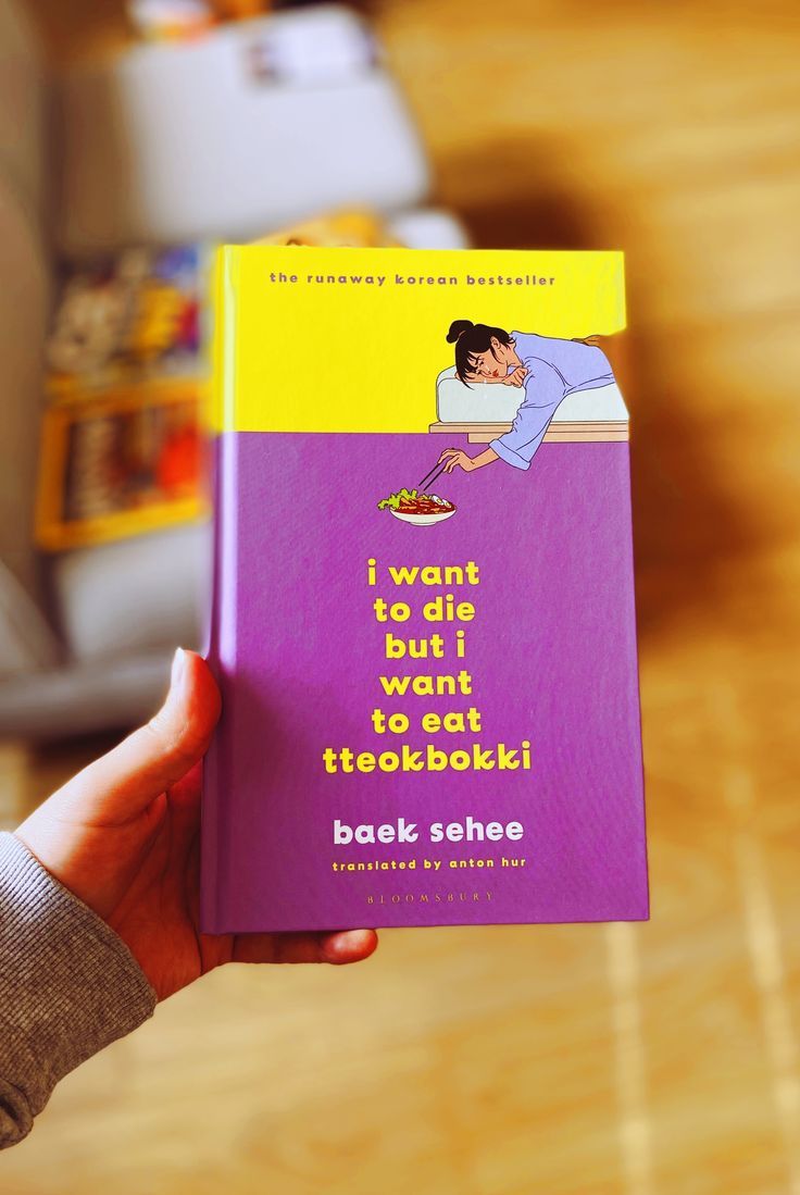 a person holding up a purple book with an image of a woman sleeping on the bed