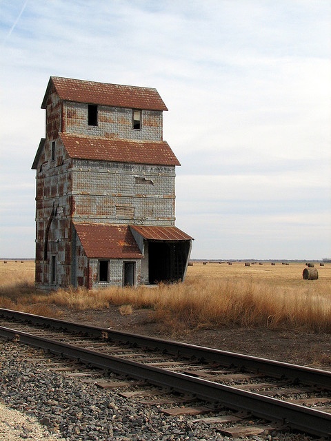 an old abandoned building sitting on the side of train tracks near a field with dry grass