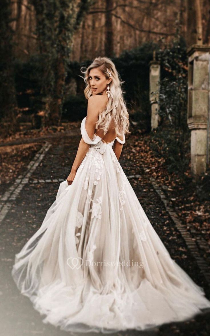 a woman in a wedding dress standing on the road with her back to the camera