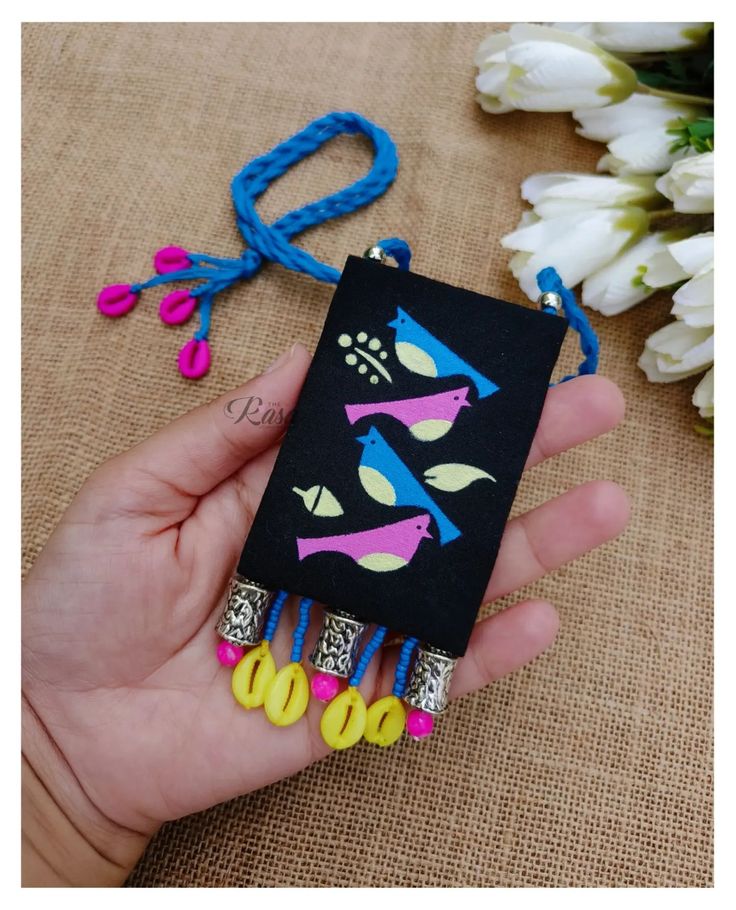 a hand holding a cell phone case with scissors and beads attached to it on a table next to flowers