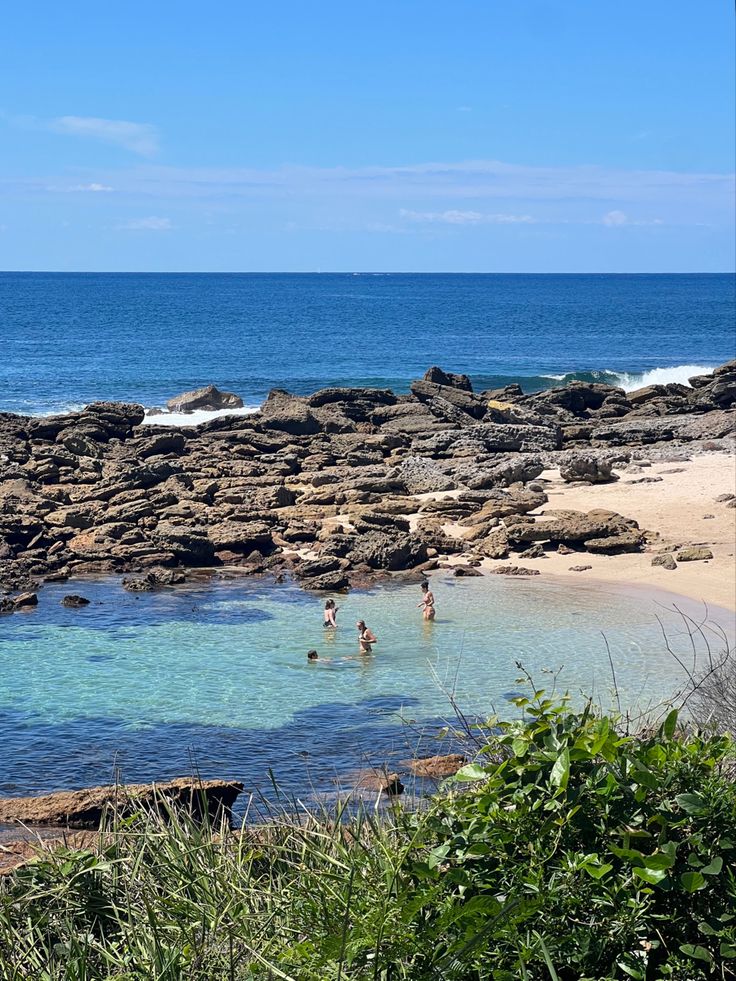 people are swimming in the ocean near some rocks