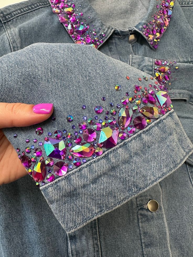 a woman's hand holding onto a jean jacket with colorful sequins on it