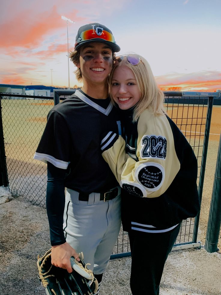 a young man and woman posing for a photo together at a baseball field with the sun setting in the background