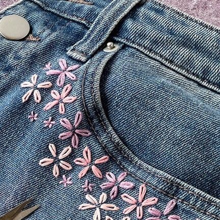 scissors are laying on the back of a pair of jeans with pink flowers embroidered on them