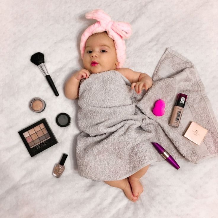 a baby laying on top of a bed next to makeup