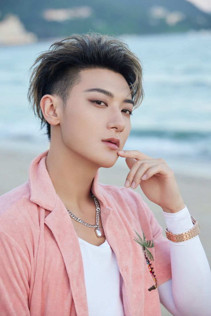 a young man wearing a pink jacket is posing for a photo on the beach with his hand under his chin