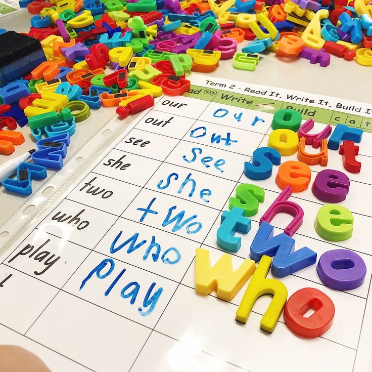 colorful plastic letters and numbers on a table with writing practice sheets in front of them