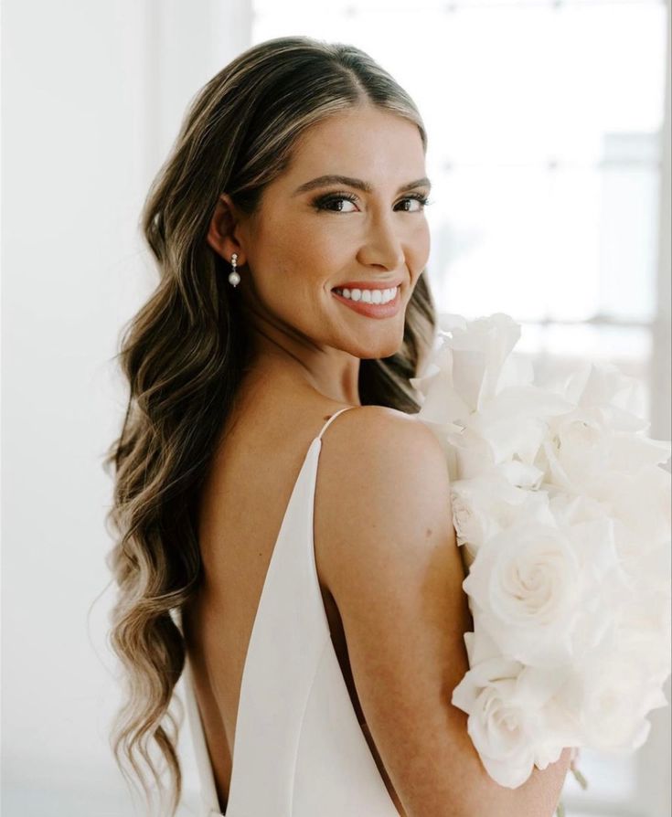 a beautiful woman in a white dress with flowers on her shoulder smiling at the camera