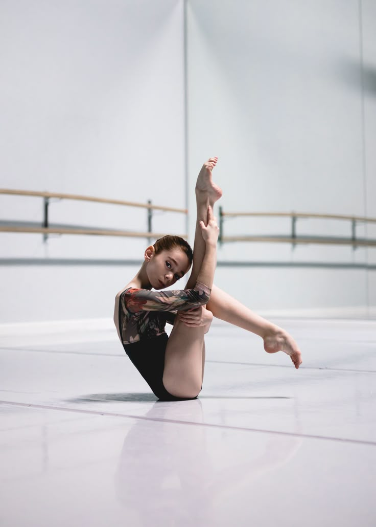 a young ballerina is sitting on the floor and stretching her leg up with one hand