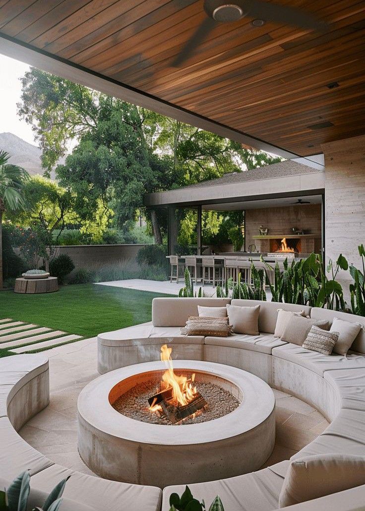 an outdoor living area with couches and fire pit in the center, surrounded by greenery