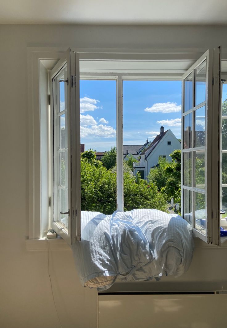 an open window with white sheets and pillows on the windowsill, looking out onto a residential neighborhood