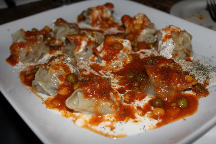 a white plate topped with dumplings covered in sauce and cheese on top of it