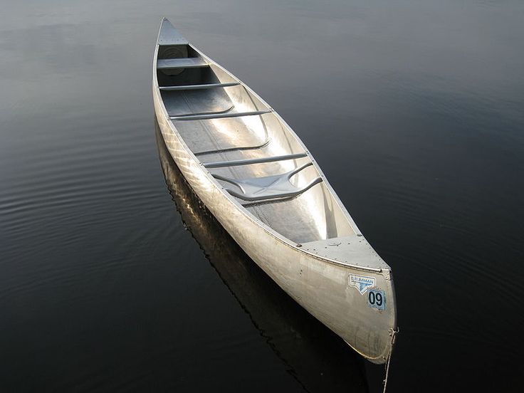 a canoe sitting on top of a lake next to a shore with no one in it