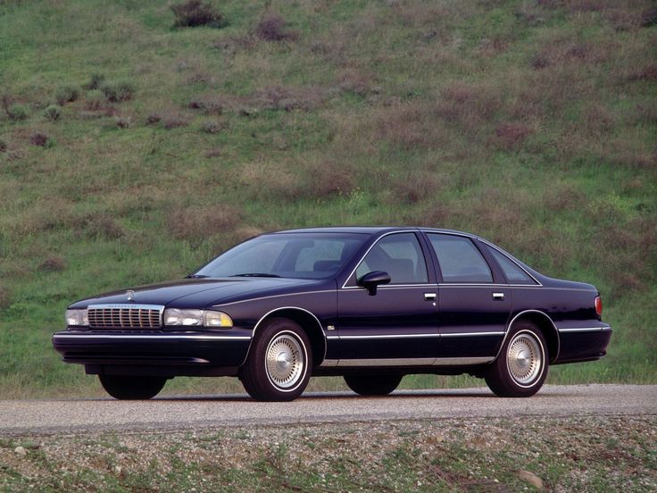 a black car parked on the side of a road next to a lush green hillside