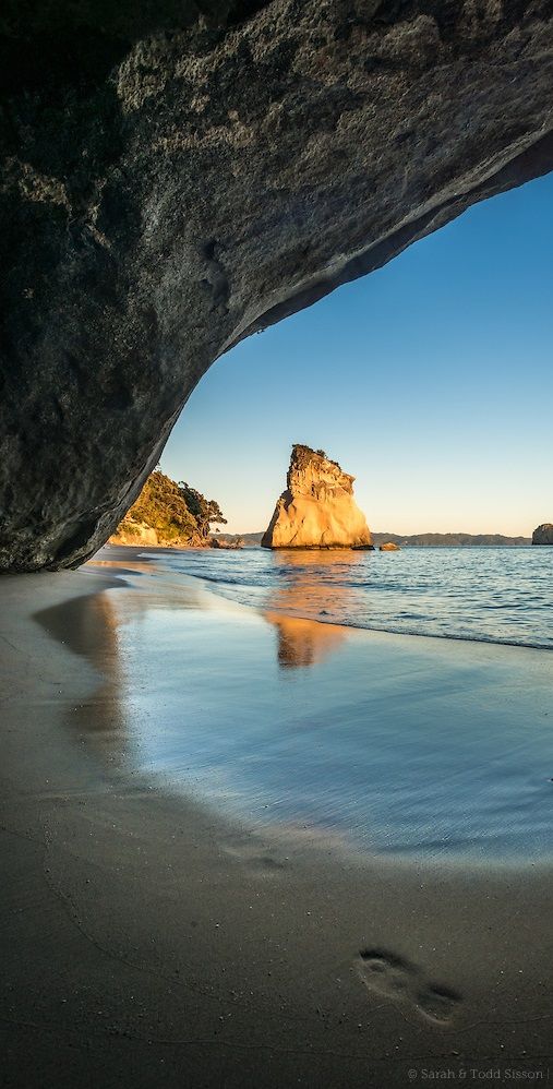 the beach is next to an arch in the rock formation that looks like it's coming out of the water