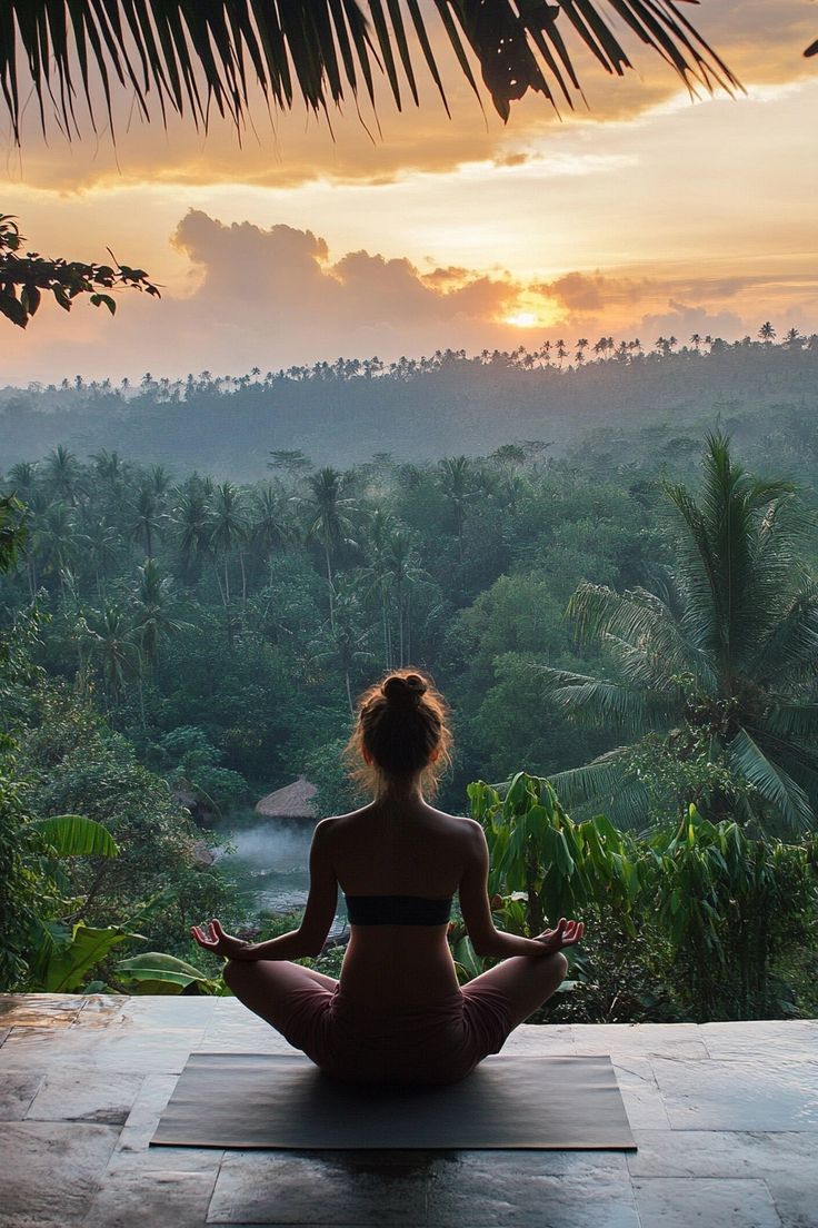 a woman sitting on top of a yoga mat in the middle of a forest at sunset