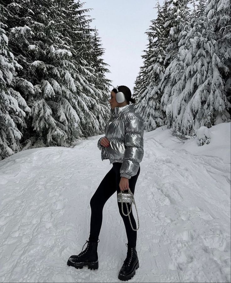 a woman is standing in the snow near some trees