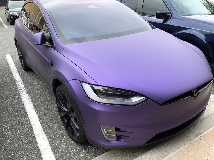 a purple car parked in a parking lot next to two other cars on the street