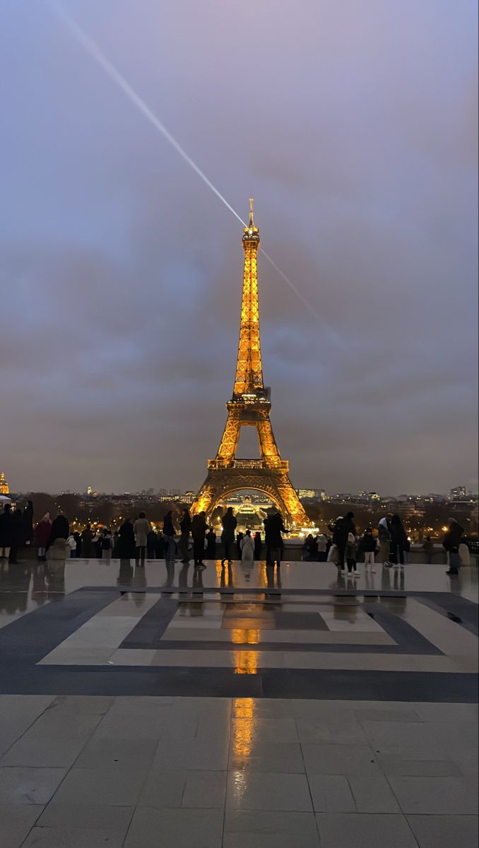 the eiffel tower lit up at night with people standing in front of it