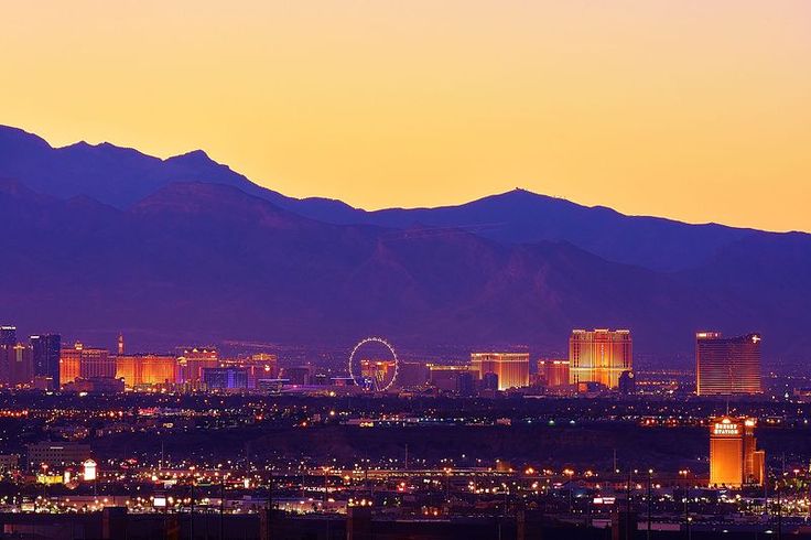 the city lights are lit up at night in front of mountains and skyscrapers,