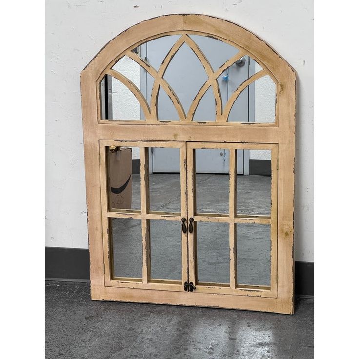 an arched wooden window with glass panes on the front and side, against a white wall