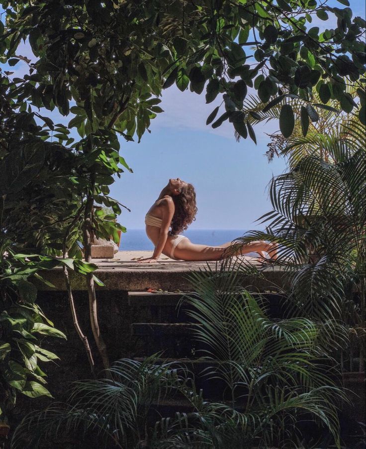 a woman is sitting on the edge of a pool in front of trees and water